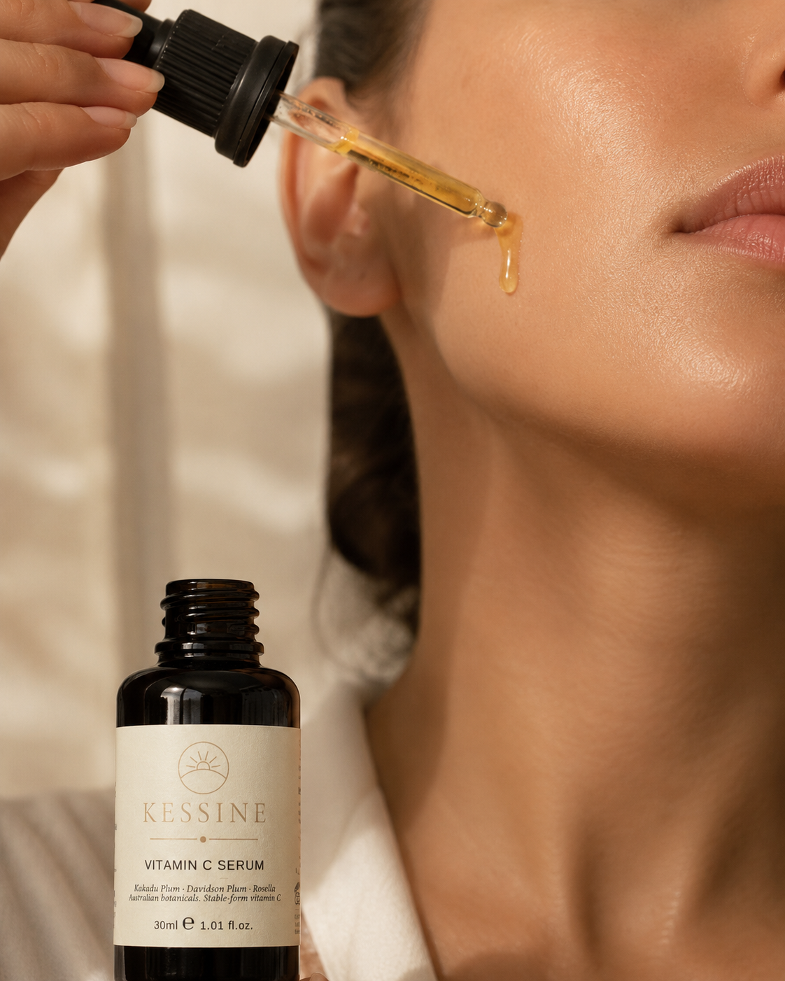A woman applying Kessine vitamin C serum to her cheek with the glass dropper